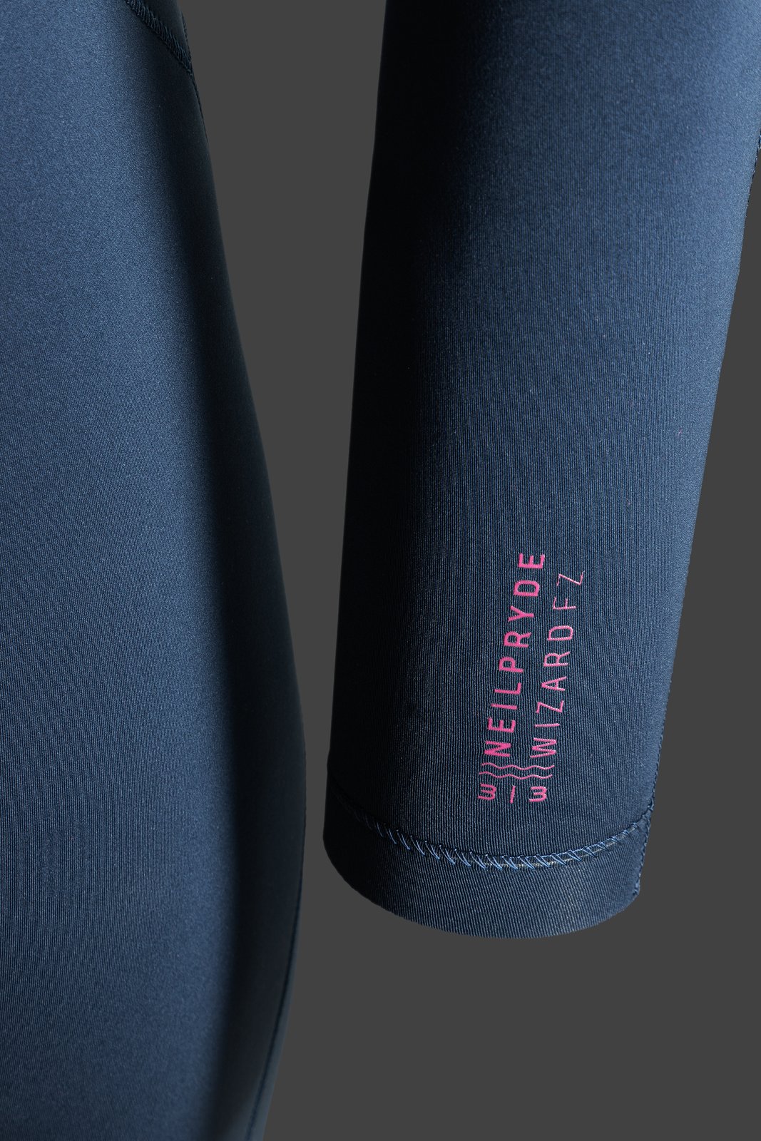 Sötétkék NeilPryde Wizard Prism 3/2 mm-es hosszú ujjú szörfruha részlete rózsaszín márkajelzéssel